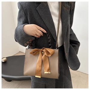 Detail of tan square handbag featuring a yellow bow and black braided handle