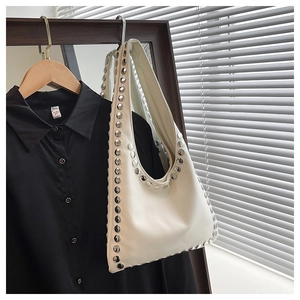 Detail shot of beige shoulder bag with large silver rivets on matte leather surface