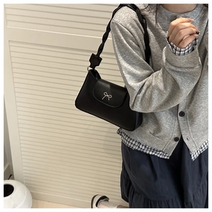 Detail of black underarm bag with silver bow accent and braided shoulder strap