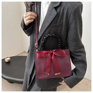Detail view of red bridal handbag with satin bow and black woven handle on model