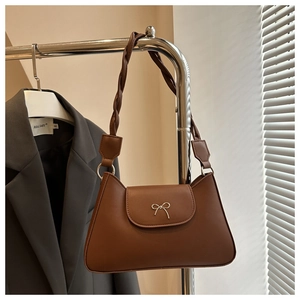 Brown faux leather underarm bag with golden bow buckle and braided strap on a hanger