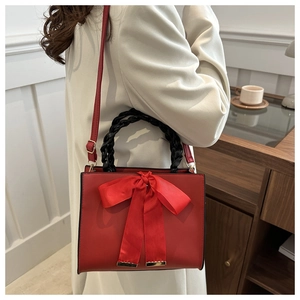 Detail of red bridal handbag with a large satin bow and woven handle on a model