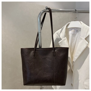 Dettaglio della grande borsa tote caffè scuro con trama in pelle vintage e logo sbalzato