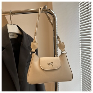 Close-up of beige shoulder bag featuring metal bow detail and braided strap texture