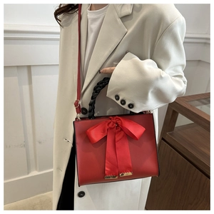Chic red handbag with a large satin bow and woven handle shown on a model