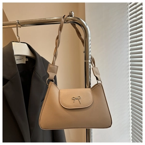 Detail of beige shoulder bag featuring a metal bow accent and woven leather strap