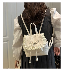 Close-up of creamy white mini backpack featuring lace trim, bow, and pearl detailing