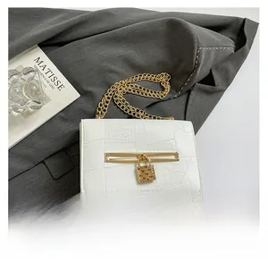 Close-up of white crocodile embossed handbag featuring a golden heart lock and chain strap