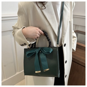 Close-up of a dark green handbag with a silk bow and black woven ring handle