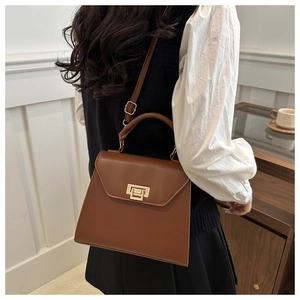 Detail of a brown trapezoid crossbody bag with a gold metal clasp shown on a model