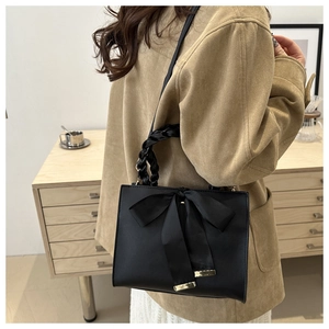 Close-up of black handbag featuring large silk bow and braided handle detail