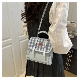 Detail of blue and white checkered handbag with red apple embroidery and dual buckle strap