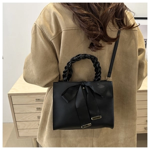 Detail of black bow handbag with braided handle and adjustable shoulder strap on a model
