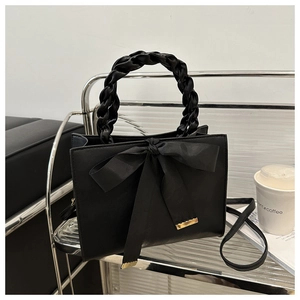 Detail of elegant black tote bag with oversized satin bow and woven handle on a shelf