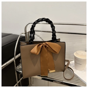 Brown leather handbag with decorative bow and black woven handle on minimalist metal shelf