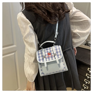 Detail of light blue plaid crossbody bag with apple motif worn by a model in interior