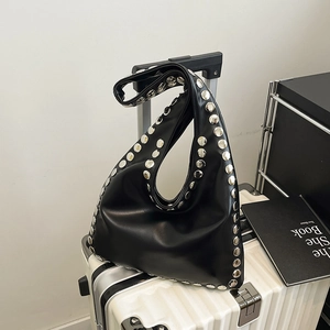 Fashionable black leather Hobo bag with silver rivets displayed on a white suitcase