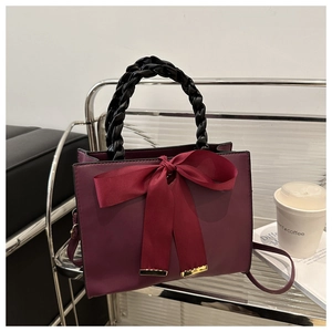 Close-up of red bridal handbag with a large ribbon bow and black woven handle detail