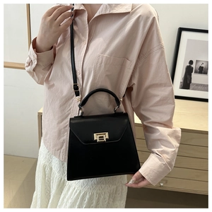 Detail of elegant black leather crossbody bag featuring a chic gold square clasp