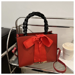 Macro shot of red square handbag featuring large bow detail and woven leather handle