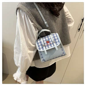 Close-up of a light blue plaid crossbody bag featuring red apple embroidery and strap detail