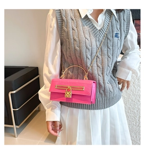 Pink croc-embossed bag with gold heart lock and handle worn on a knit vest