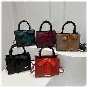 Multiple colors of woven handle handbags with silk ribbon bows on white display stands