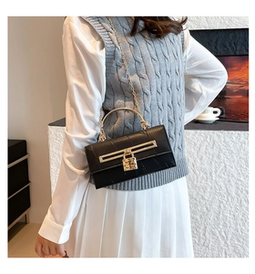 Detail of black crocodile embossed kelly bag with gold clasp and chain strap on a model