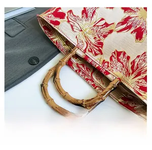 Detail of red and gold floral embroidery on tote bag with natural bamboo handles