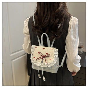 Detail view of light blue leather backpack featuring lace trim and red ribbon bows
