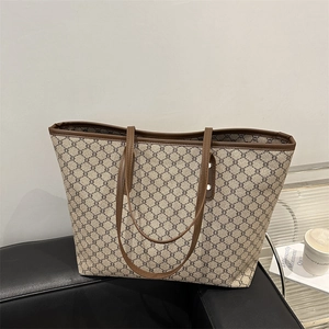 Classic triomphe pattern tote bag with leather straps on a modern leather bench