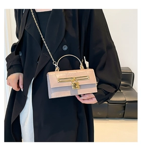 Detail of crocodile textured crossbody bag with gold lock and chain on a black coat