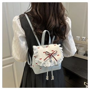 Close-up of cream bow backpack with red prints, lace edges, and heart pendant detail