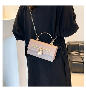 Close-up of beige croc-effect handbag with gold heart lock and metal handle detail