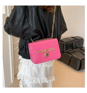 Detail of fuchsia crocodile texture handbag with gold chain strap on a model shoulder