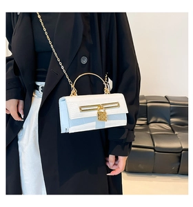 Detail of white crocodile pattern handbag with gold handle and chain on black coat