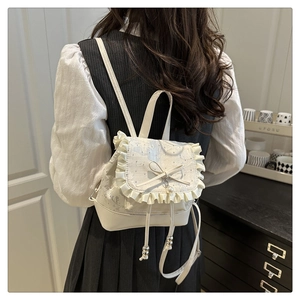 Detail of white mini backpack with lace edges, bow pearl pendant, and silver bead drawstring