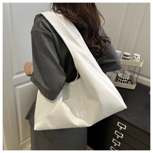 Close-up of a large white glossy leather shoulder bag worn by a model in a home setting