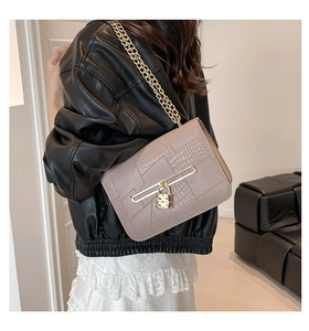Detail shot of beige faux crocodile chain bag on model in a minimalist modern setting