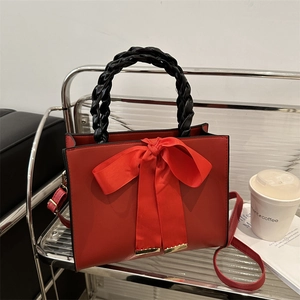 Red bow handbag with black woven handles and adjustable shoulder strap for women