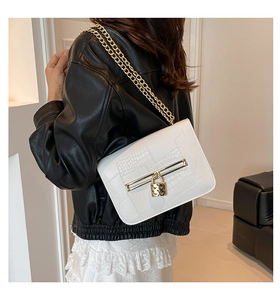 Detail of white crocodile embossed leather bag with gold heart lock and chain strap
