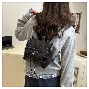 Detail of black mini backpack featuring lace polka dots, ruffles and a pearl bow charm