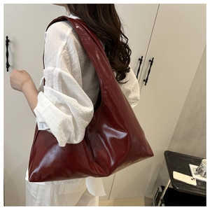 Side view of large burgundy tote bag in glossy faux leather on model's shoulder