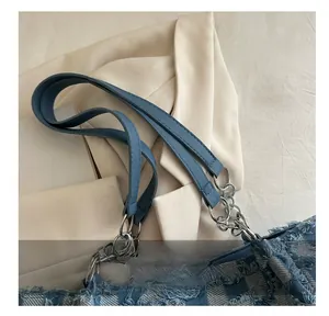 Detail of blue denim tote with quilted texture and silver chain strap attachment