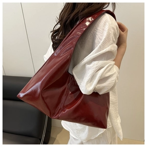 Detail of burgundy glossy leather shoulder bag with wide strap on model back view