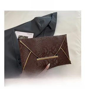 Détail d'une pochette enveloppe marron à texture serpent avec fermoir en métal doré