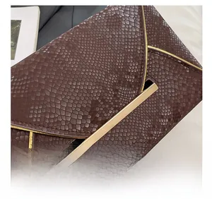 Gros plan sur la pochette enveloppe en cuir serpent marron avec détails métalliques dorés