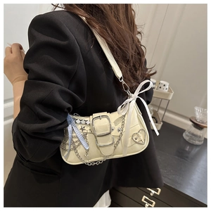 Detail of cream Y2K shoulder bag with metal chain, heart buckle, and silk bow decorations