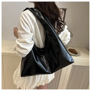 Chic black glossy hobo bag with large capacity shown on shoulder in minimalist interior
