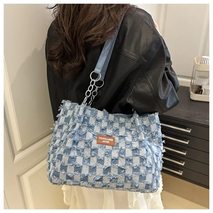 Detail of blue checkerboard tote bag with distressed frayed edges and chain strap